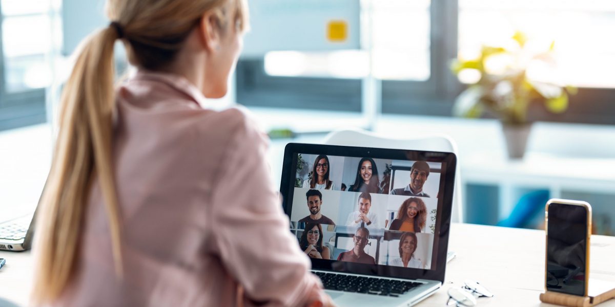 Back view of female employee speaking on video call with diverse colleagues on online briefing with laptop at home.